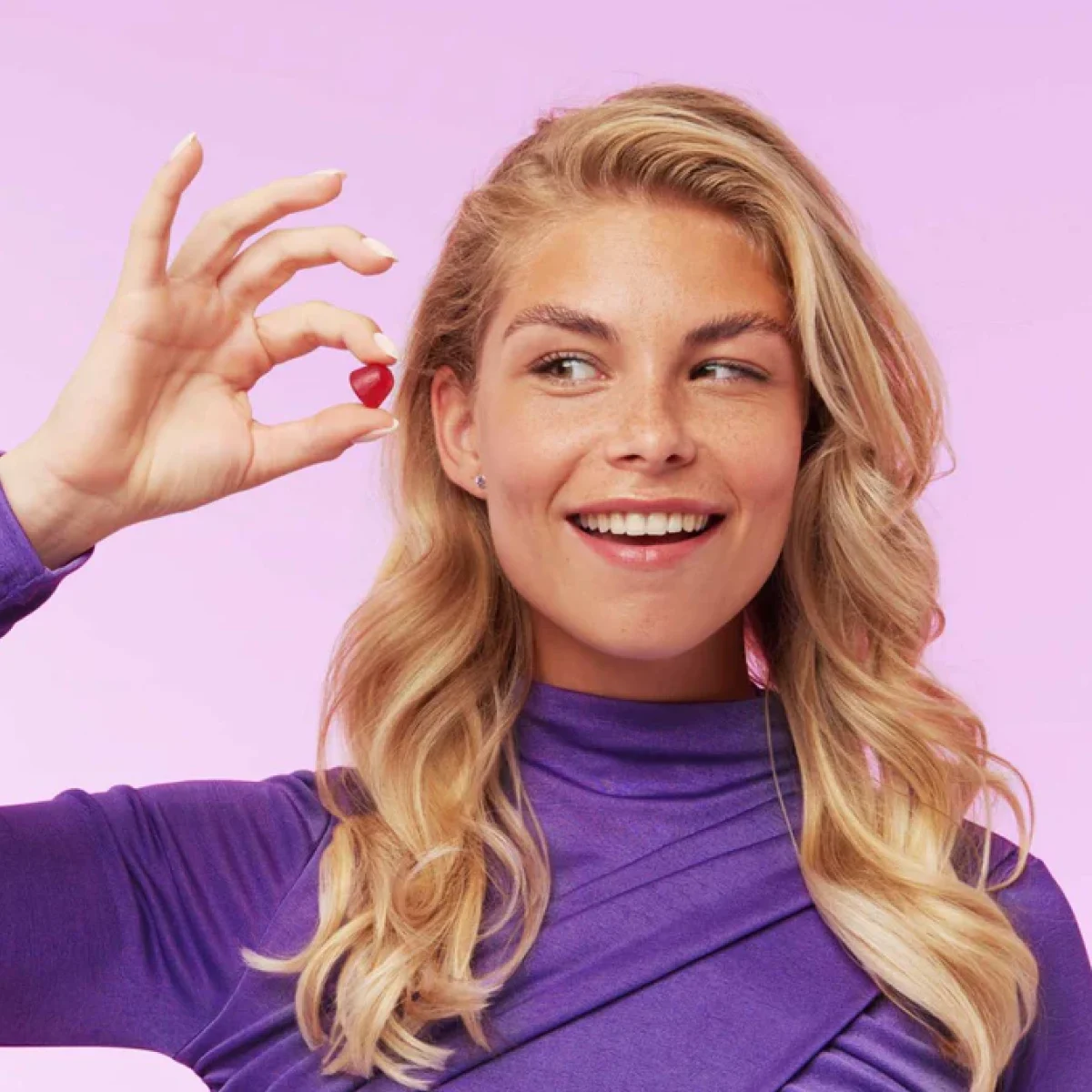 Woman holding a red Yummygums vitamin gummy up to her face