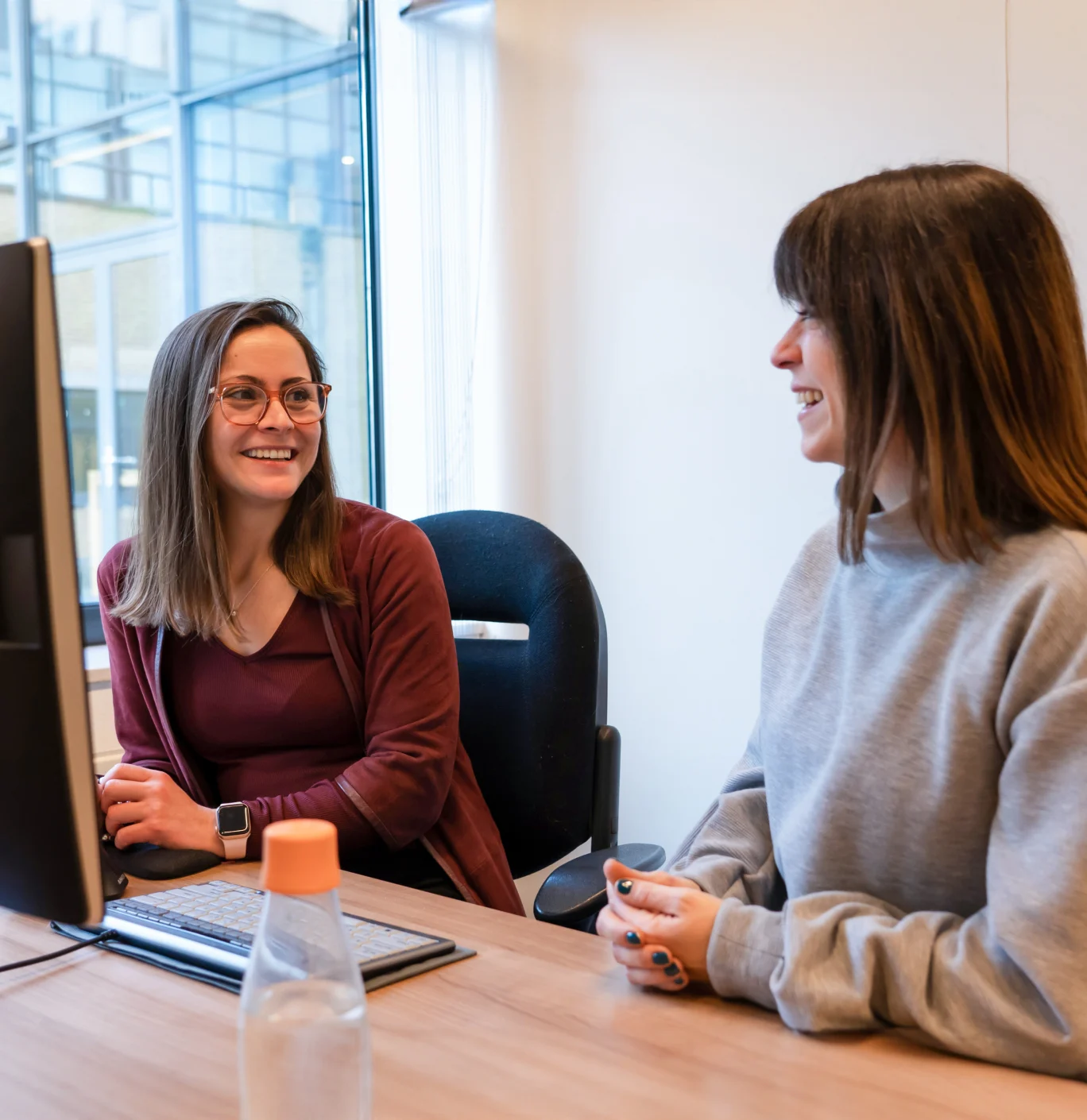 Twee collega’s die samen aan een bureau in een licht kantoor over een project praten