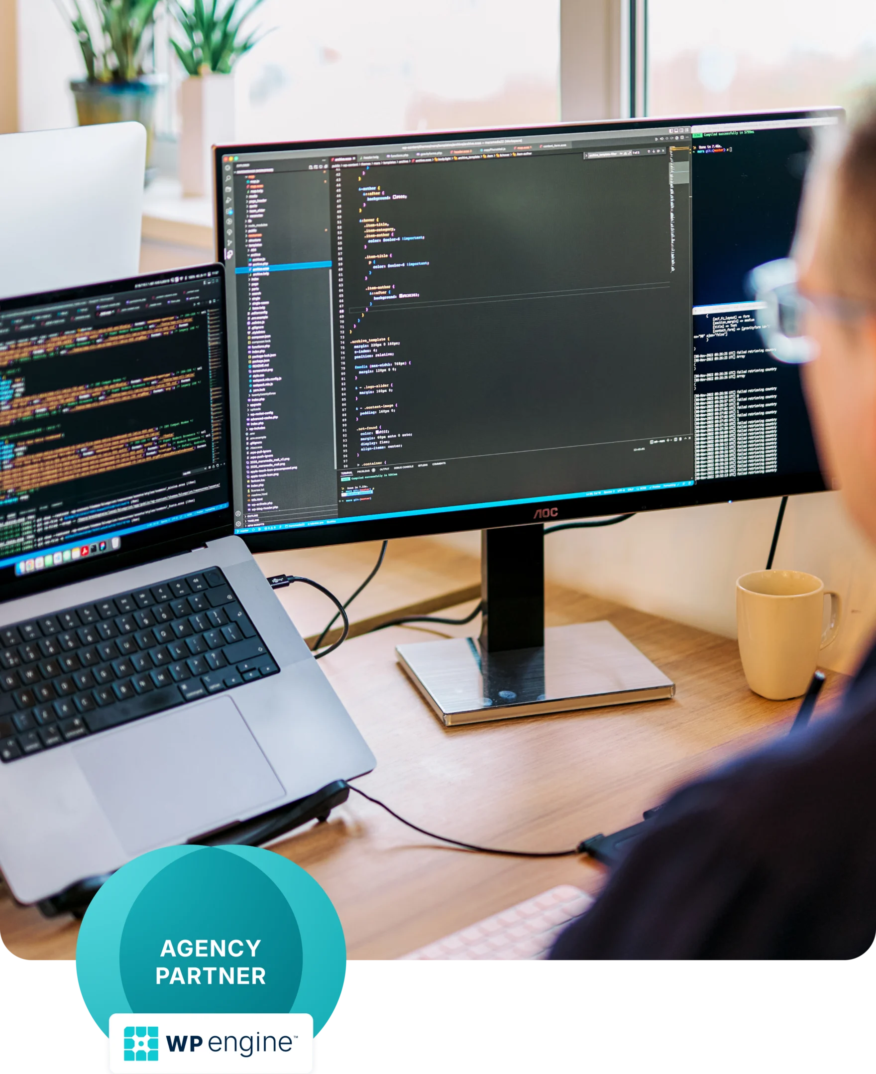 Developer's desk with monitors showing WordPress code and a WP Engine Agency Partner badge