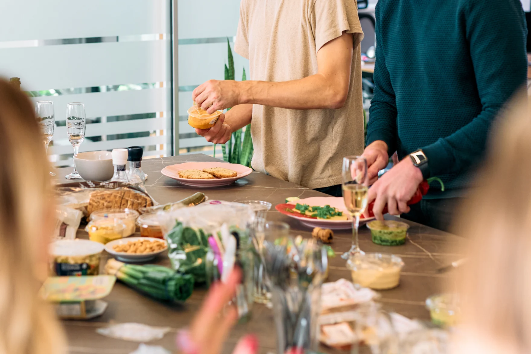 Colleagues preparing a wrap lunch spread with fresh toppings, dips and sparkling wine
