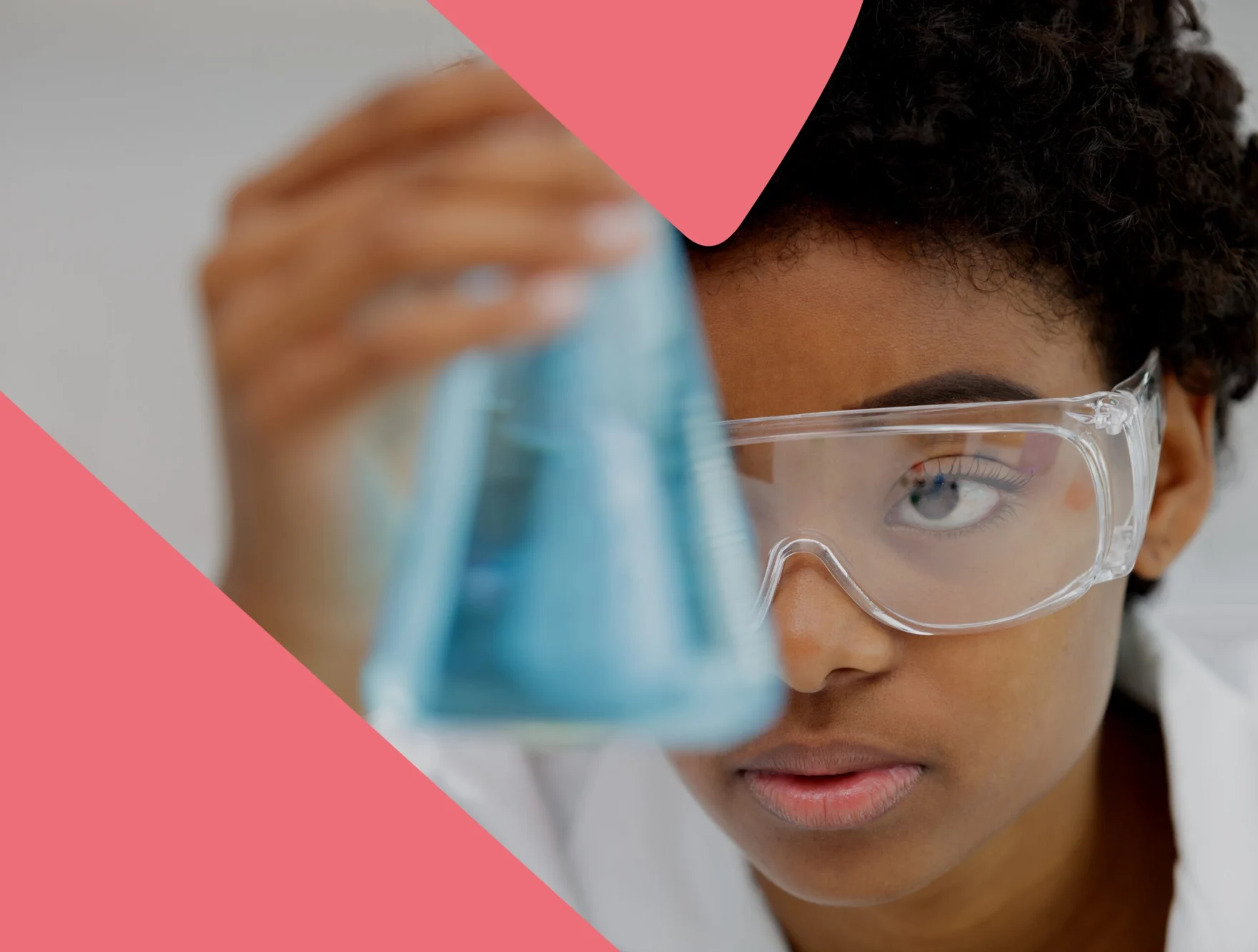 Scientist in a lab coat wearing safety goggles, holding up a blue liquid-filled flask
