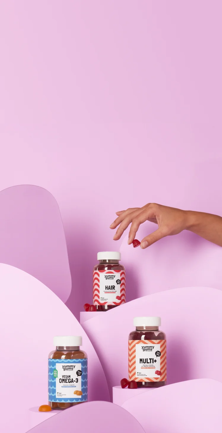 Flesjes met Yummygums-vitaminegummies, uitgestald op een roze trapvormig rek, met een hand die ernaar reikt