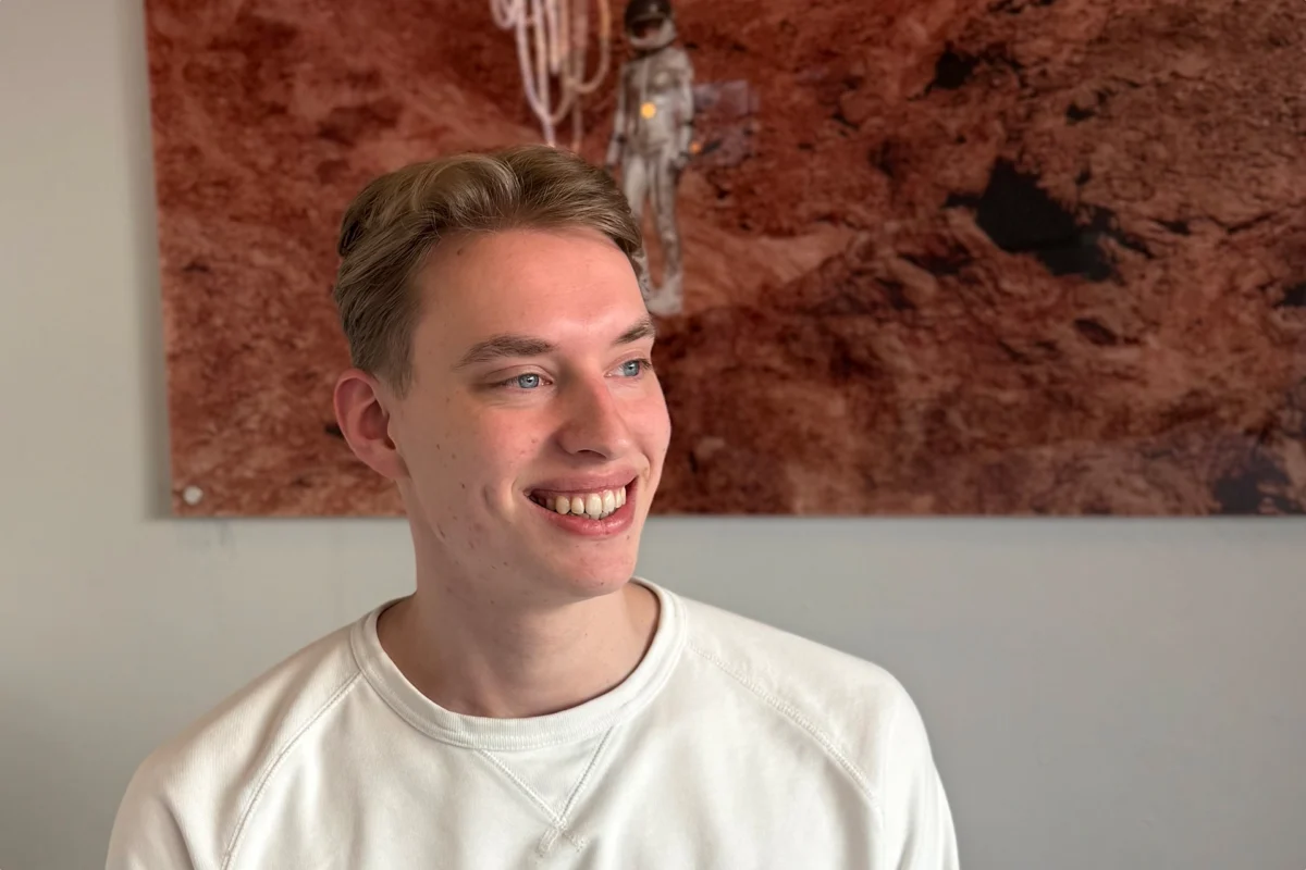 Young man in white sweatshirt smiling and looking right with reddish-brown textured background.